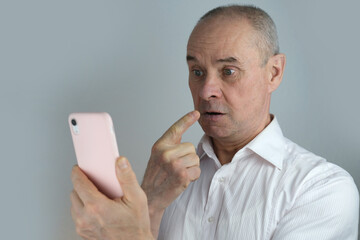 close-up of mature charismatic man looks at screen of phone in pink cover, senior 60 years...