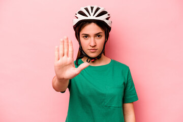 Young caucasian woman wearing helmet isolated on pink background standing with outstretched hand showing stop sign, preventing you.