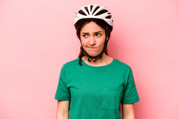 Young caucasian woman wearing helmet isolated on pink background confused, feels doubtful and unsure.