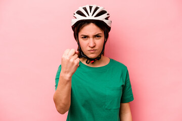Young caucasian woman wearing helmet isolated on pink background showing fist to camera, aggressive facial expression.