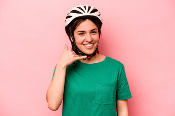 Young caucasian woman wearing helmet isolated on pink background showing a mobile phone call gesture with fingers.