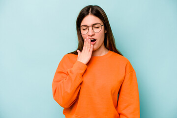 Young caucasian woman isolated on blue background yawning showing a tired gesture covering mouth with hand.