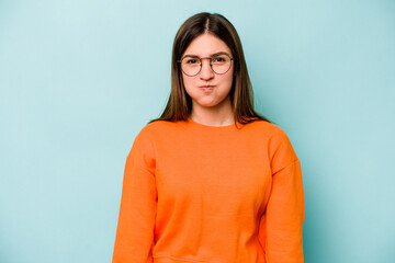 Fototapeta premium Young caucasian woman isolated on blue background blows cheeks, has tired expression. Facial expression concept.