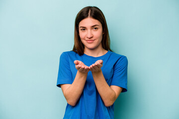 Young caucasian woman isolated on blue background holding something with palms, offering to camera.