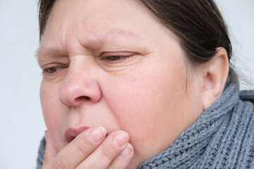 close-up of mature woman 55 years face, sick person with inflamed eyes holding on to sore throat,...