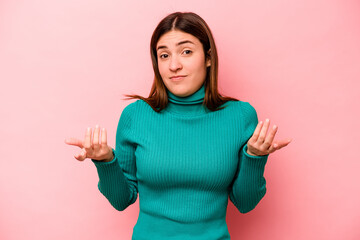 Young caucasian woman isolated on pink background doubting and shrugging shoulders in questioning...