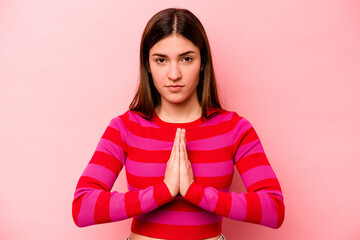 Obraz premium Young caucasian woman isolated on pink background praying, showing devotion, religious person looking for divine inspiration.