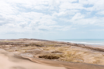 View of the sand and dunes in front of the sea with some clouds in the sky. 