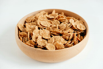 Crispy healthy dry cereal flakes in a wooden bowl on white background