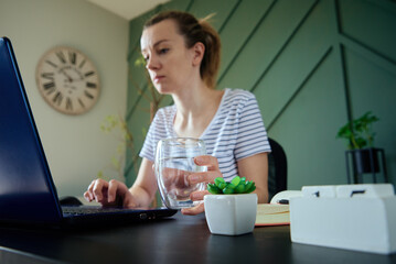 Woman holds glass of water while working remotely at home office, Healthy care for freelancer work