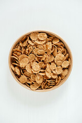 Crispy healthy dry cereal flakes in a wooden bowl on white background
