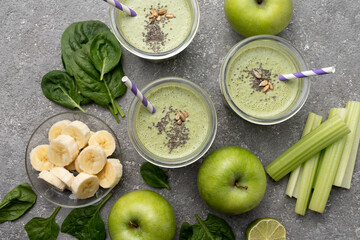 Healthy green spinach smoothie in glass jars and other ingredients on a gray concrete background. Superfoods, detox, diet, healthy food. Celery, apple, spinach, spinach, and banana.