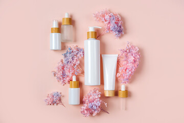 Cosmetic bottles mockups with flowers for branding and packaging presentation. Pump bottle, cream tube, and dropper on pastel background. Natural skincare beauty product concept.