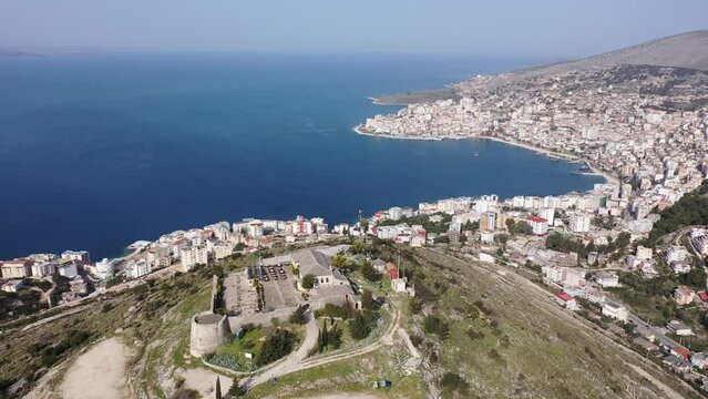 Scenic aerial view of Sarande cityscape on shores of gulf of Ionian Sea and ancient Lekuresi Castle on hill above city on sunny spring day, Albania