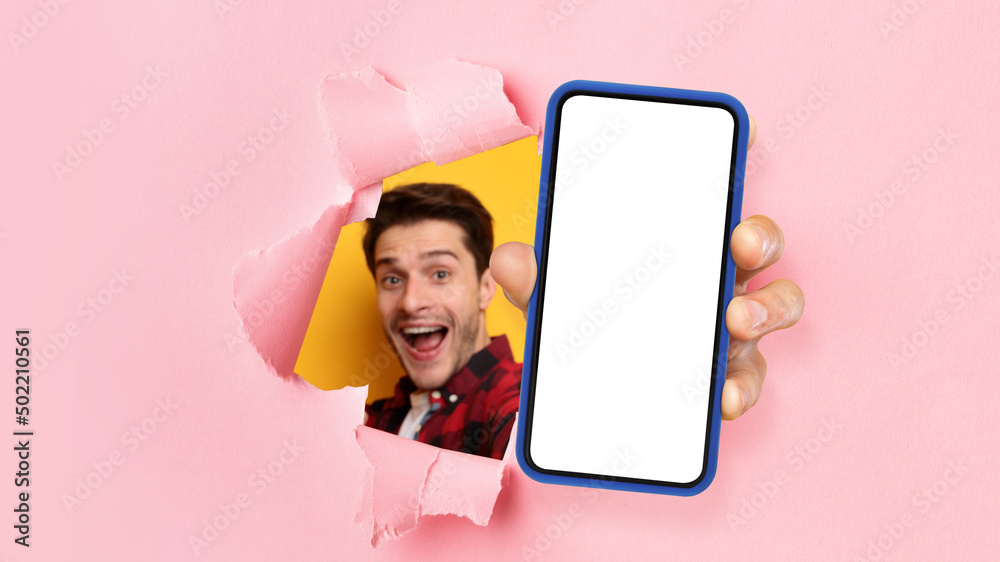 Poster excited guy showing white empty smartphone screen through torn paper