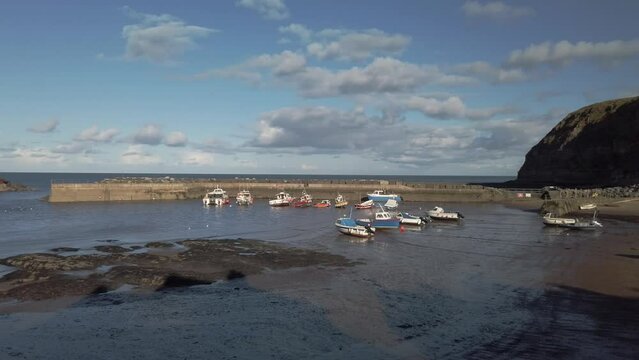 Fishing boats at low tide and the harbour in Staithes, Yorkshire. Pan left