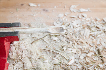 Selbst geschnitzter Holzlöffel eingespannt im Schraubstock bearbeitet mit Messer Werkzeug auf einer Werkbank mit Holzspäne, Deutschland - obrazy, fototapety, plakaty