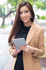 Strong working Asian business woman on duty with computer tablet in green urban street