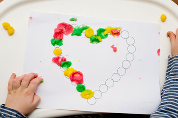 Making Valentines greeting card for mummy. little boy applying play dough on printed paper heart. fine motor skills, finger coordination. early education for babies