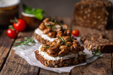 Whole grain rye bread toast with cream cheese or ricotta, mushroom and herbs on rustic wooden background.