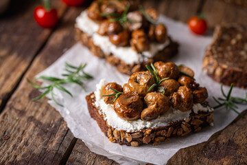 Obraz na płótnie Canvas Whole grain rye bread toast with cream cheese or ricotta, mushroom and herbs on rustic wooden background.