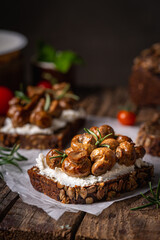 Whole grain rye bread toast with cream cheese or ricotta, mushroom and herbs on rustic wooden background.