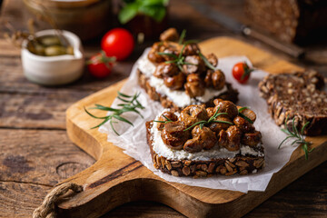 Whole grain rye bread toast with cream cheese or ricotta, mushroom and herbs on rustic wooden background.