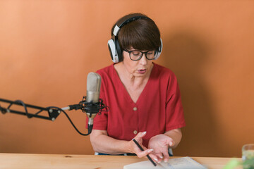 Mature woman making podcast recording for her online show. Attractive business woman using...