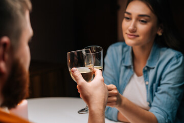Close-up back view of happy young couple clinking glasses with champagne at table in cozy dark restaurant. Loving man and woman celebrating anniversary, Valentines day, enjoying romantic date.