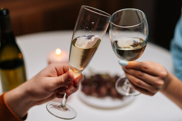 Close-up high-angle view of happy couple clinking glasses with wine at table with candles in cozy dark room. Loving man and woman celebrating anniversary, Valentines day, enjoying romantic date.