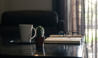 Open notebook, cup and glasses on the table, blurred background.