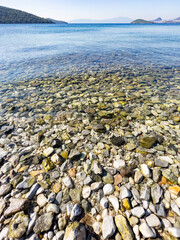 Close-up of wet stones and sea. Pebbles beach. Tiny rocks in crystal clear saltwater. Horizon over water on sunny day. Sky reflecting on waves. Vertical background with copy space