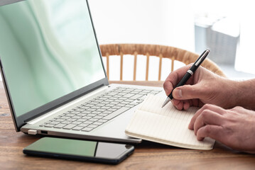 man taking notes on paper while using laptop computer, e-learning or working from home concept