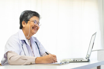 Asian doctor woman using a laptop computer and writing something on clipboard at hospital desk office, Healthcare medical concept.