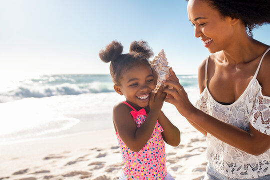 Cute Little Black Girl Listening To Shell At Beach With Her Mom