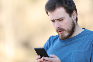 Confused man checking smart phone outdoors