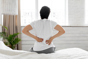 Man suffering from back pain at home in bedroom