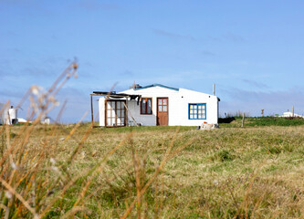 Fototapeta na wymiar Simple house, white construction in Uruguay, grass, department of Cabo Polonio. Coastal city, coastline, beach. Housing in desert space, sparsely inhabited. Undergrowth, sunny day. Paradise view.
