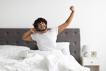 Well-rested indian guy in pajamas stretching in bed