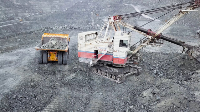 Top view of excavator in open pit. Excavator falls asleep rubble in dumper on outdoor quarry in extraction of minerals. Concept of extraction of minerals