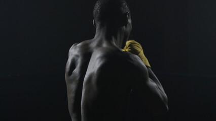 Rear view of muscular man boxing on black background. Afro american young male boxer practicing...
