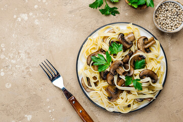 Cooked pasta with mushrooms with parsley on plate on beige stone kitchen table background, top...