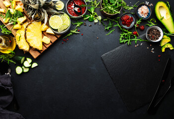 Healthy eating food layout and diet nutrition concept. Pineapple, vegetables, dried fruits, greens and other ingredients for salad preparation on black table background with slate board