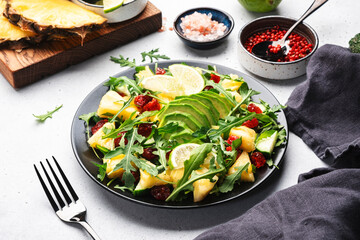 Summer vegan salad with juicy pineapple, fresh arugula, avocado and dried cranberry on white stone kitchen table, top view. Healthy eating, clean diet food, weight loss concept