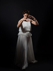 An ancient heroine, a young woman in the image of an ancient Greek goddess or muse. A noble heroine in a white tunic and a laurel wreath, dancing on a black background