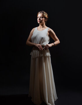 An ancient heroine, a young woman in the image of an ancient Greek goddess or muse. A noble heroine in a white tunic and a laurel wreath, a full-length photo on a black background