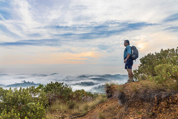 Naklejka na ściany i meble Hiker Asian man standing on peak of mountain admiring cloud scape and sunrise