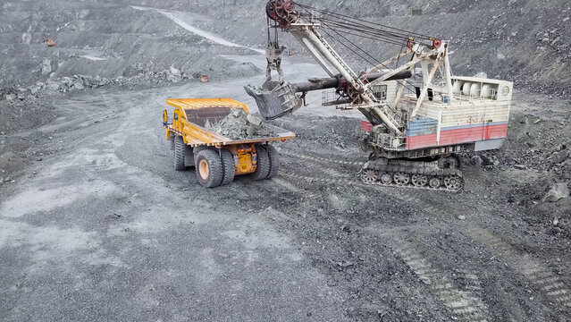 Top view of excavator in open pit. Excavator falls asleep rubble in dumper on outdoor quarry in extraction of minerals. Concept of extraction of minerals