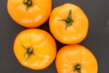 Four organic yellow tomatoes on a slate stone, close up, top view.