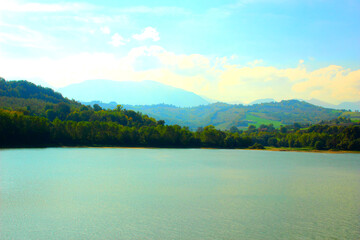 Beautiful San Ruffino lake surrounded by hills covered with green trees under the blue sky with some clouds during a sunny autumn day